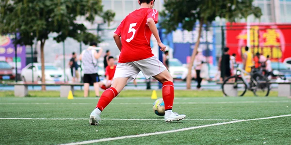 Un étudiant dans un maillot rouge frappe un ballon de soccer sur l'aire de jeux